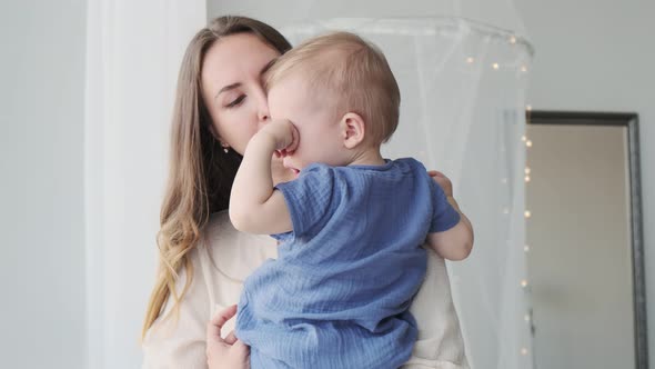 Close-up of a beautiful loving mother in a dress, who is standing at the window with a baby in her a