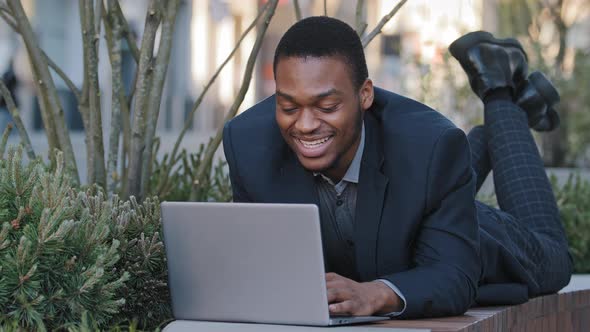 Smiling Confident Satisfied Young Adult Businessman or Corporate Employee Lying Down Uses Laptop