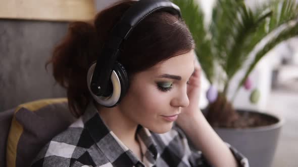 A Brunette Girl with a Beautiful Makeup Puts on Headphones and Listens with Pleasure to Her Favorite
