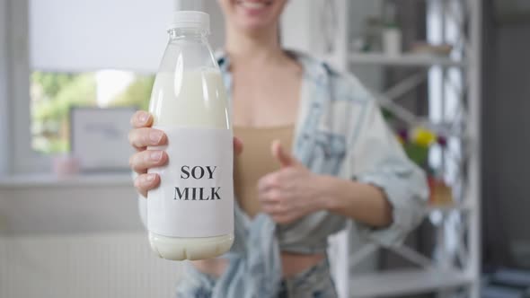 Closeup Soy Milk Bottle with Blurred Unrecognizable Caucasian Woman Gesturing Thumb Up Smiling at