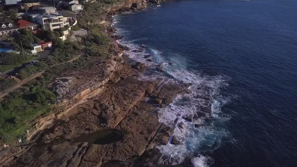 Aerial Drone shot of beautiful waterfront houses near a park and cliff with ocean waves crashing on