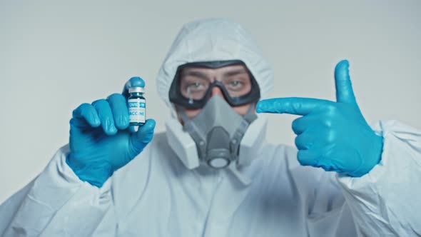 Doctor in a Protective Suit Shows a Developed Vaccine and Thumb Up. Concept of Global Pandemic