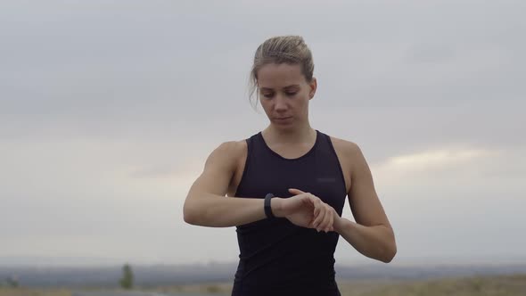 Athletic Woman in an Outdoor Sports Uniform Looks at Smart Watch on Hand Checking Her Indicators and