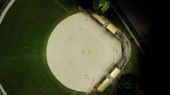 Aerial Drone Footage Of Baseball Field At Night With People Playing Baseball On Grass Field