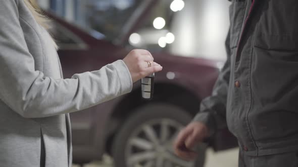 Female Caucasian Hand Passing Car Keys To Male Auto Mechanic in Repair Shop. Unrecognizable Woman