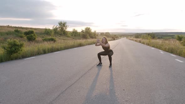 Young Athletic Girl Training Squats with Fitness Elastic Band on Road at Nature