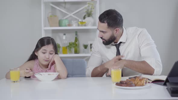 Hurrying Middle Eastern Businessman Talking To Little Girl Eating Breakfast and Pointing at Watch