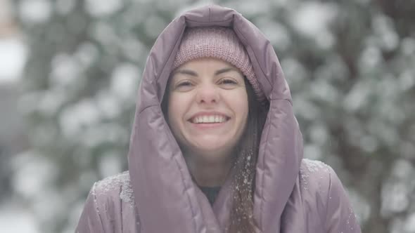 Closeup Portrait of Happy Slim Young Caucasian Woman Tossing Snow and Smiling Looking at Camera