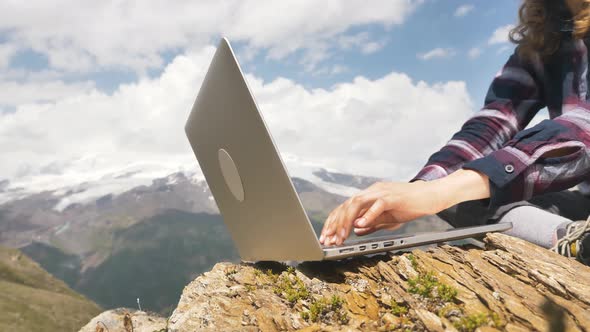 Female Hands Closeup Working at a Laptop on a Large Stone Against the Background of Mountains a