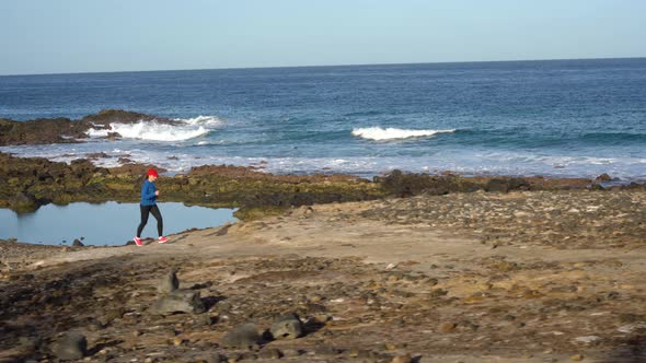 Woman Runs Along the Stony Shore of the Ocean