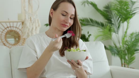 Happy Brunette is Relaxing on the Couch and Eating a Vegetable Salad at Home