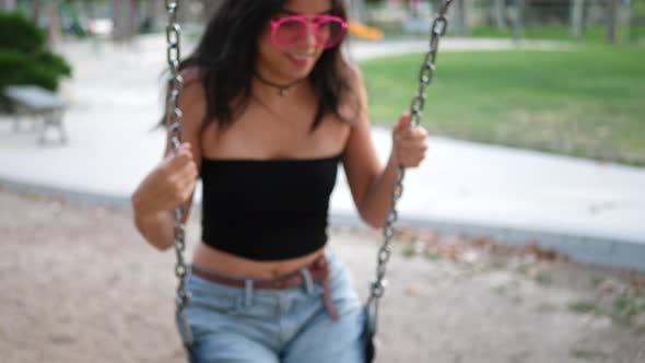Close up on a pretty hispanic girl playing and having fun on the playground swing set wearing retro