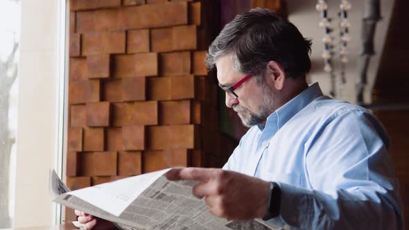 Senior Man Spending Time in Cafe Reading Newspaper