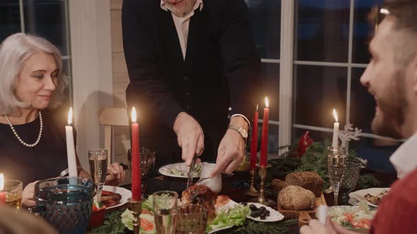 Grandad Cuts and Serves Chicken on Table on Christmas Eve Everybody Chatting