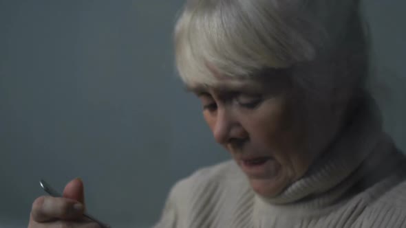 Upset Senior Woman Eating Tasteless Porridge Near Rainy Window in Nursing Home