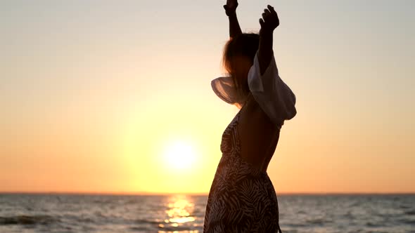 Free Girl with Long Hair in a White Shirt Dances in the Sunset. Healthy Woman Dancing on the Beach.