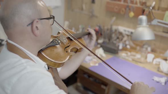 Luthier master playing violin in workshop