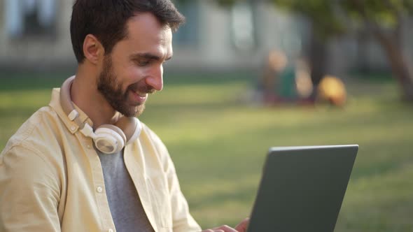 Smiling Male Student with Laptop Studying Outdoors