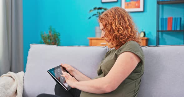 Pregnant Girl is Relaxing in Living Room on Couch with Tablet