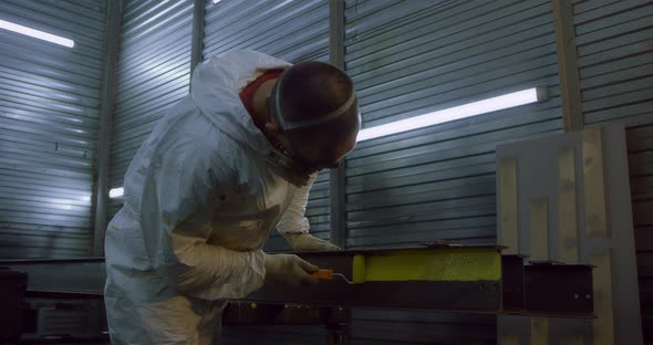Man in Overalls and Protective Mask Paints Metal Structures with a Roller Yellow
