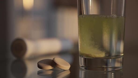 Effervescent tablet dissolves in a glass of water. Vitamin C pills on the table