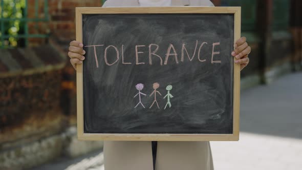 Woman Arms Holding and Raising Schoolboard with Tolerance Text Message on Street Close Up