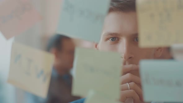 a Thoughtful Young Businessman Looks at the Wall with Stickers and a Wall for Writing and Planning