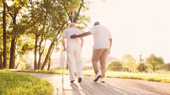 African-American caregiver is teaching disabled old man to walk with walker. Nurse and patient.