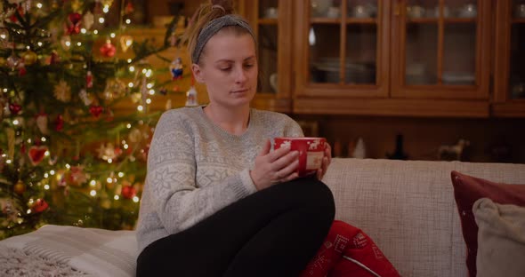 Woman Relaxing on a Sofa Holding Mug and Drink Hot Tea at Christmas Evening