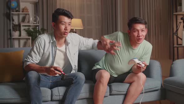 Young Asian Friends Playing Video Games At Home. Have Fun Together With Joysticks In Hands