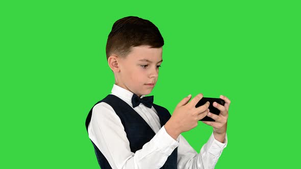 Concentrated Boy in a White Shirt Bow Tie and Vest Watching Something on His Phone on a Green Screen