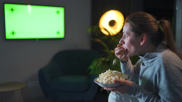 Woman Sitting on a Sofa in the Living Room in the Evening and Watching a Green TV Screen Mockup is