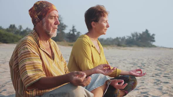 Senior Couple Sits and Meditating Together on Sandy Beach