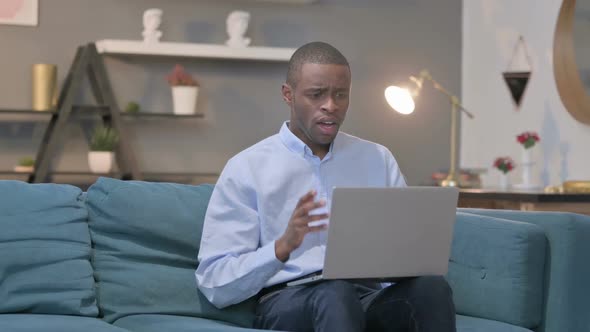 African Man with Laptop Reacting to Loss on Sofa