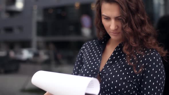 Young Business Woman Looking at Documents with a Serious Look Near Office Building
