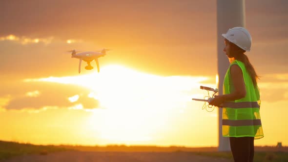 Woman Ecology engineer holding joystick controlling flying drone working windmill beautiful sunset