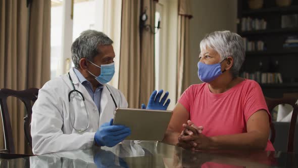 Male doctor visiting senior mixed race woman, consultation using tablet