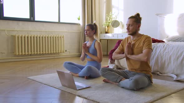 Young Couple is Meditating in Bedroom in Front of Laptop Monitor