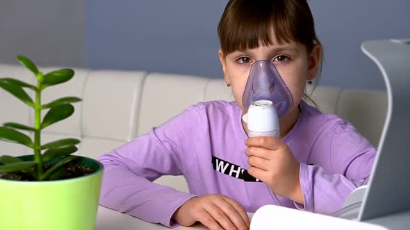 Little Girl Makes Inhalation with Medical Nebulizer While Sitting at the Table Looking to Camera