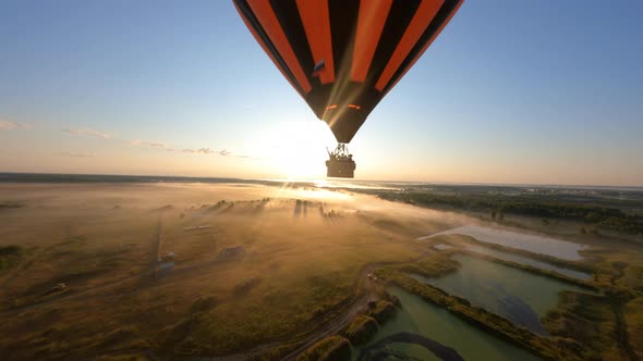 hot air ballon floating above sloping field at beautiful sunrise