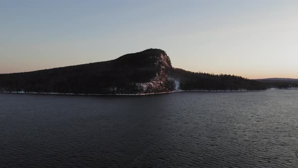 Rising up above a cold winter lake with a lone mountain in the distance at dawn AERIAL