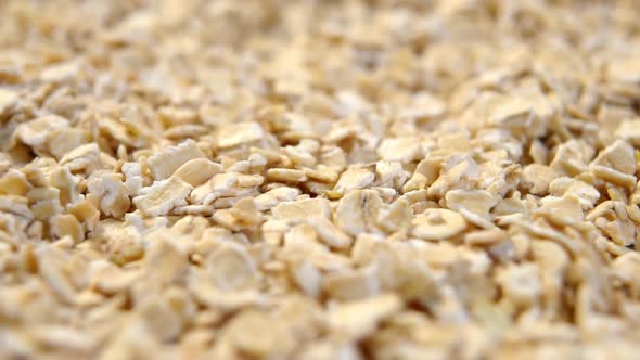 Rolled crushed oatmeal. Falling flakes in slow motion close-up. Cereal raw morning porridge