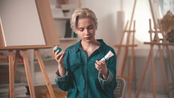 A Young Woman Artist Looking at Two Different Tubes of a Blue Paint