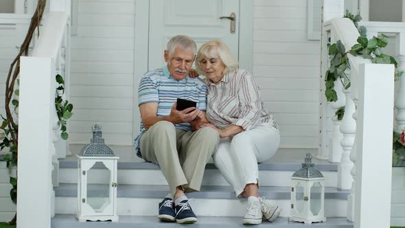 Senior Elderly Caucasian Couple Using Digital Tablet in Porch at Home. Enjoy Online Shopping, News