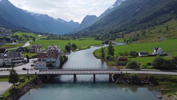 Tourists traveling through Olden city center over concrete bridge - closeup forward moving aerial -