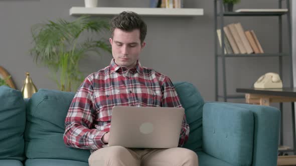 Man with Laptop Smiling at Camera on Sofa