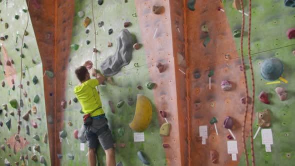 Male Climber Climbs the Cliff Wall in the Room Reaching and Gripping Hold