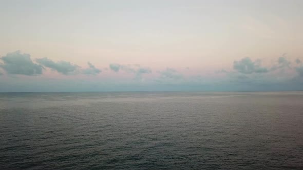 Soft pink color of dawn over the sea in Thailand. Small waves, clouds reflected in the water.