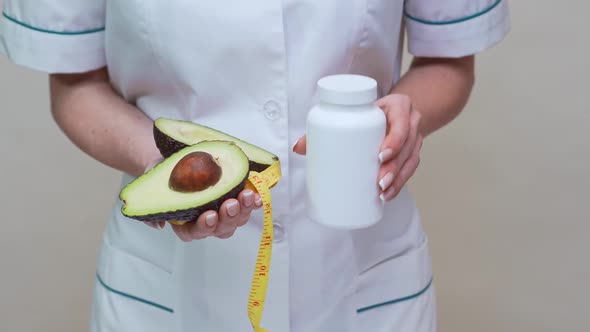 Nutritionist Doctor Holding Organic Avocado Fruit and Jar of Medicine or Vitamin or Omega 3 Capsules