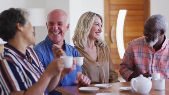 Two diverse senior couples sitting by a table drinking tea together at home